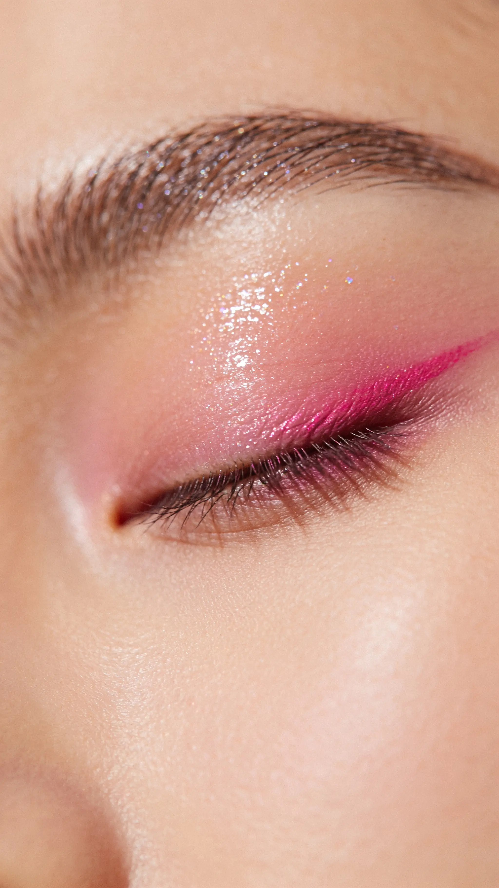 Primo piano di un occhio chiuso con make up rosa e fucsia e pelle luminosa